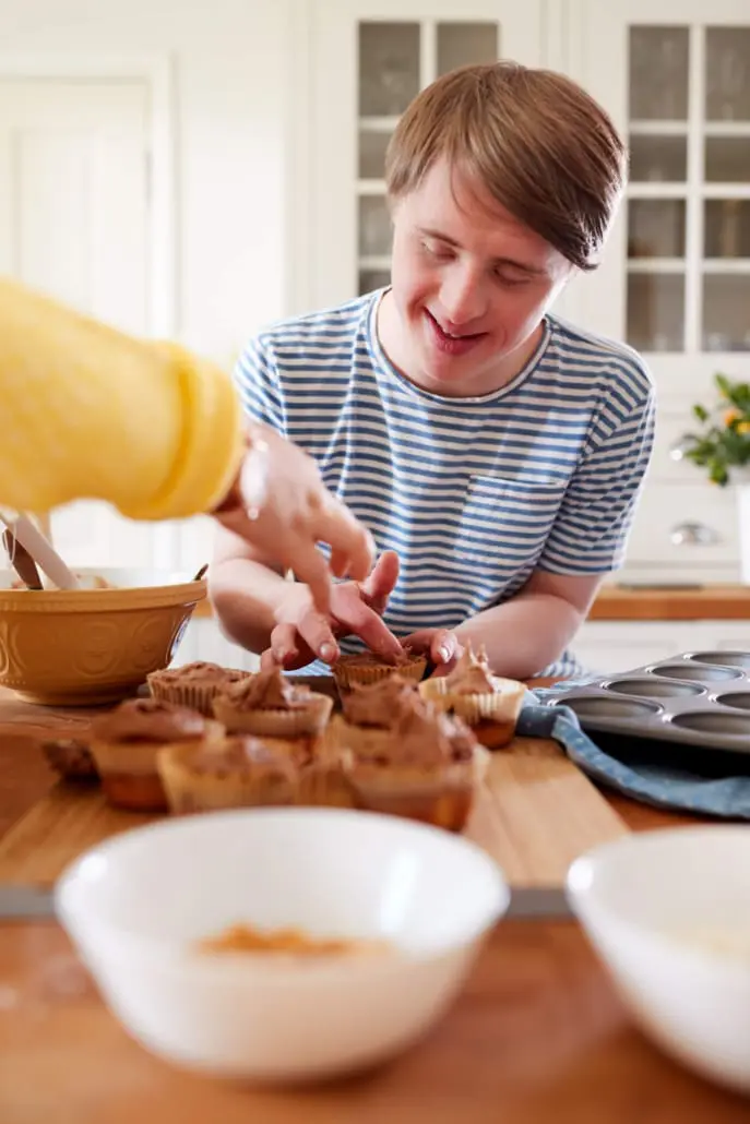 Young man with Down syndrome icing muffins in a home kitchen
