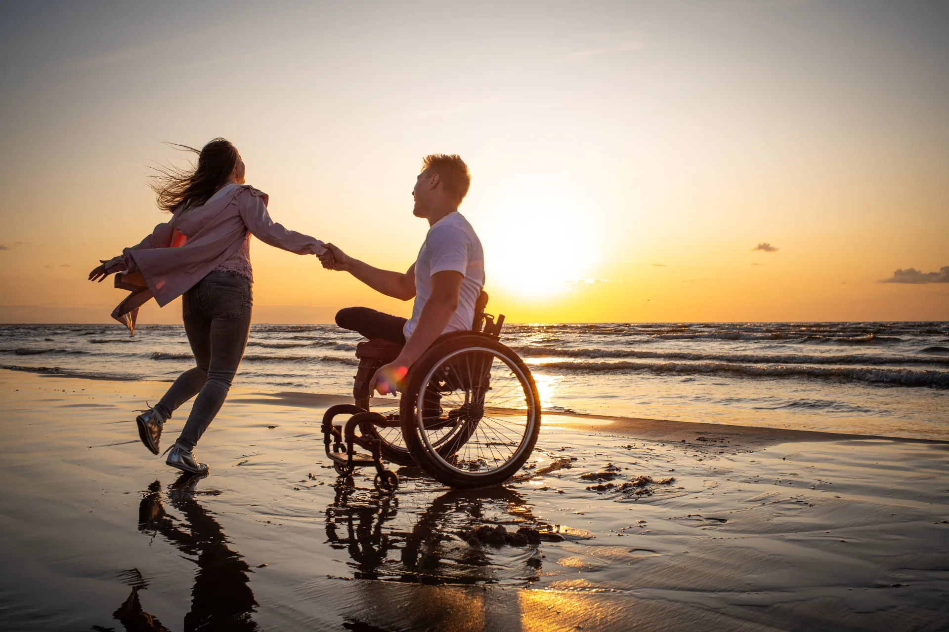 Couple at the beach at sunset, one person using a wheelchair