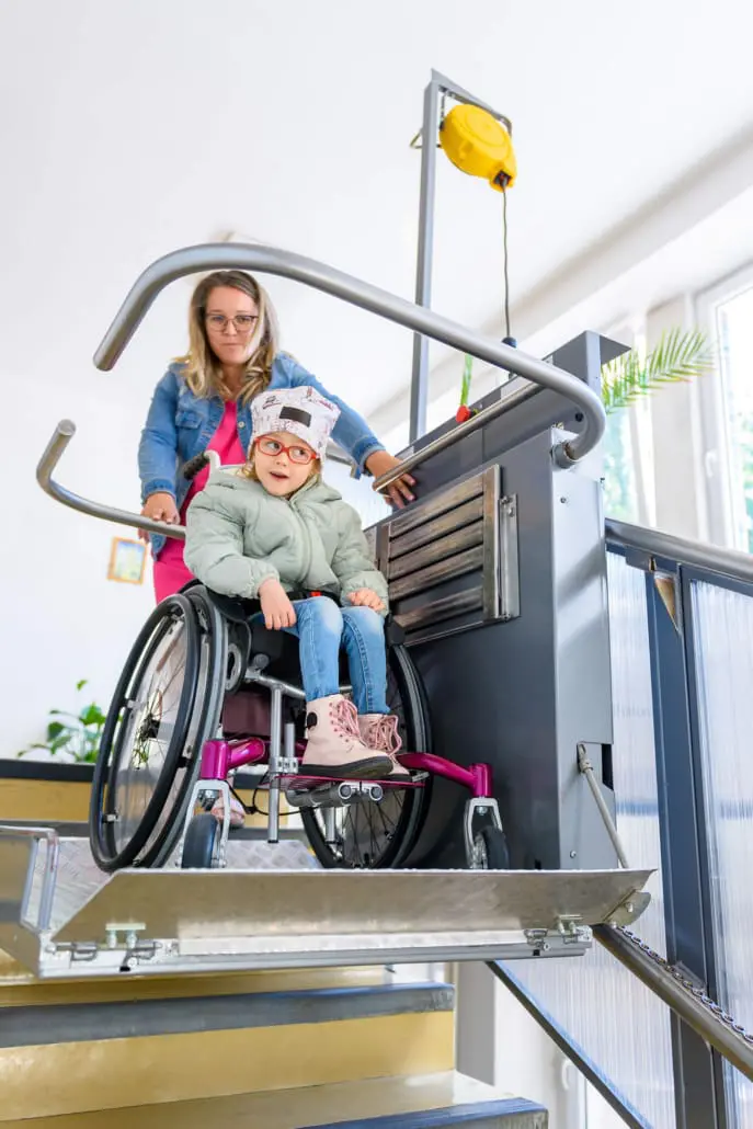 Young girl in a wheelchair using an accessible platform lift with her mother