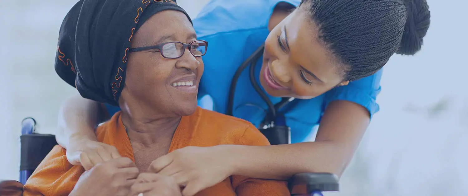 Community nurse smiling with an older woman seated in a wheelchair during a home care visit