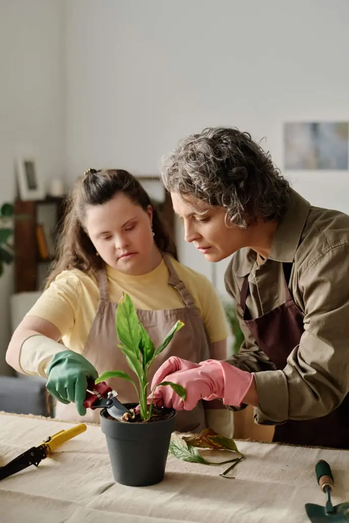 Young woman with Down syndrome repotting a plant alongside her support worker