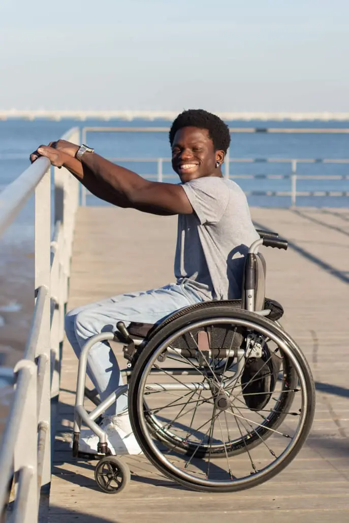 Young man in a wheelchair smiling on a boardwalk beside the water
